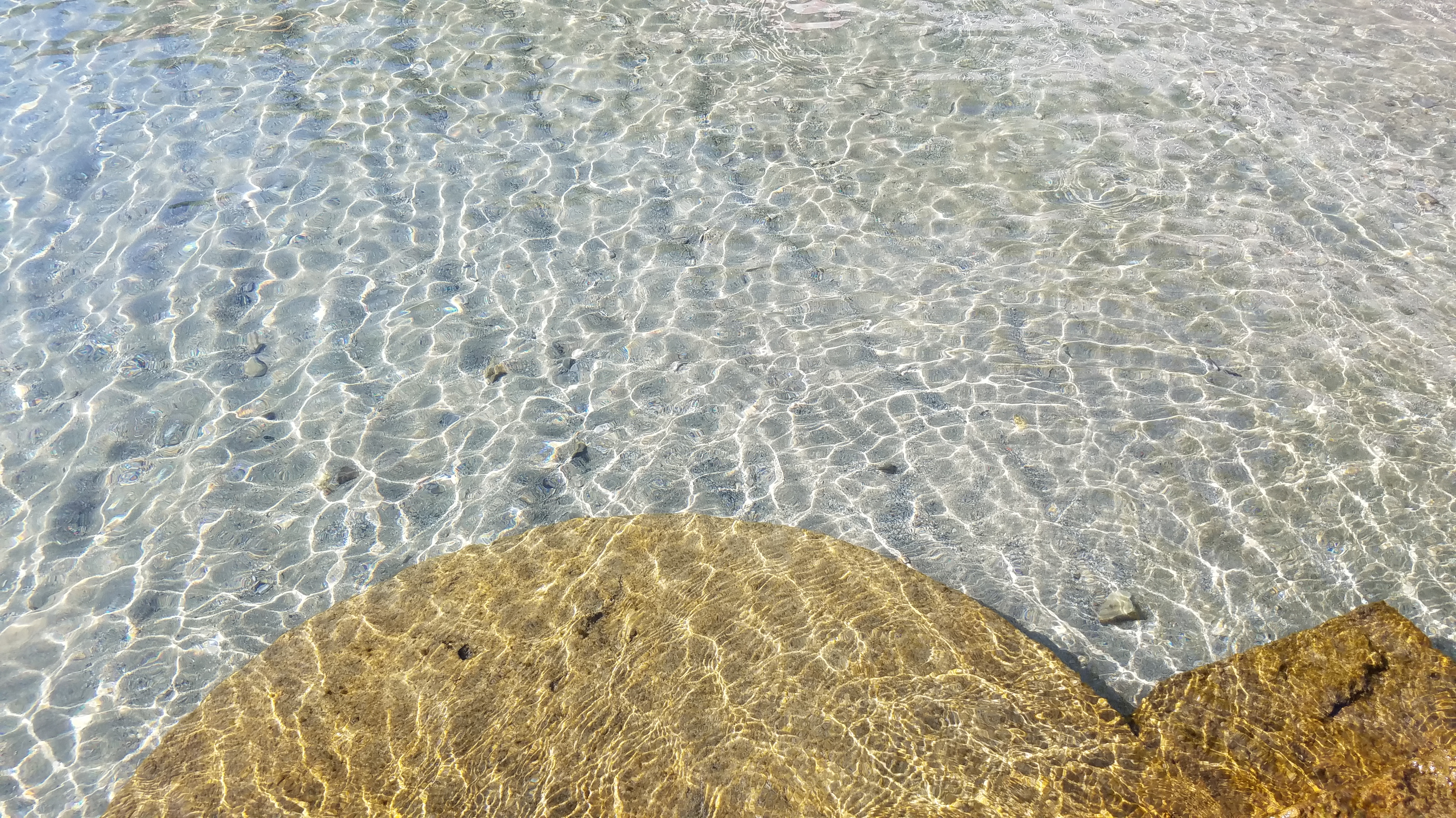 Sunlight rippling through clear shallow water over golden stone